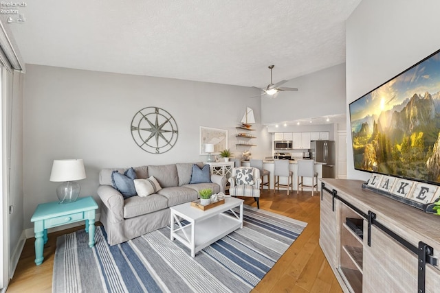 living area featuring high vaulted ceiling, light wood-style flooring, a ceiling fan, and a textured ceiling