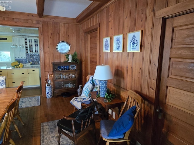 living area with crown molding, beamed ceiling, wood finished floors, and wooden walls