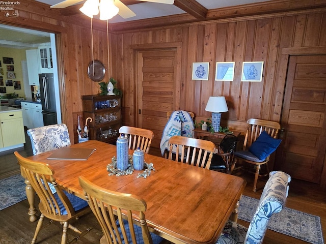 dining space with wood walls, ceiling fan, wood finished floors, and beamed ceiling