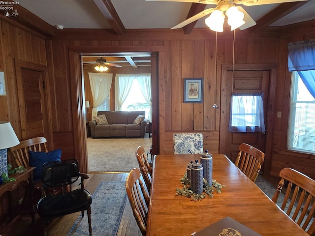 dining space with a wealth of natural light, wood walls, wood finished floors, and beam ceiling