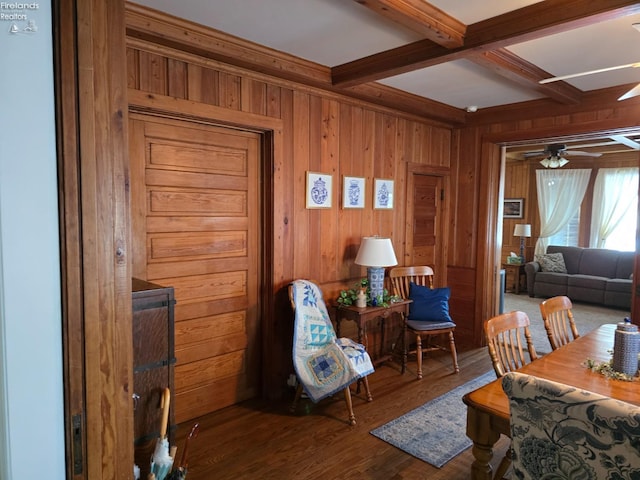 dining room with wooden walls, coffered ceiling, ceiling fan, beamed ceiling, and wood finished floors