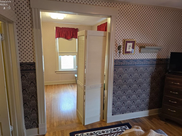 corridor with baseboards, crown molding, wood finished floors, and wallpapered walls