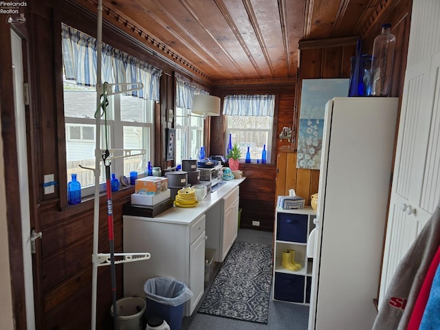 kitchen featuring wooden walls, wood ceiling, freestanding refrigerator, light countertops, and white cabinetry