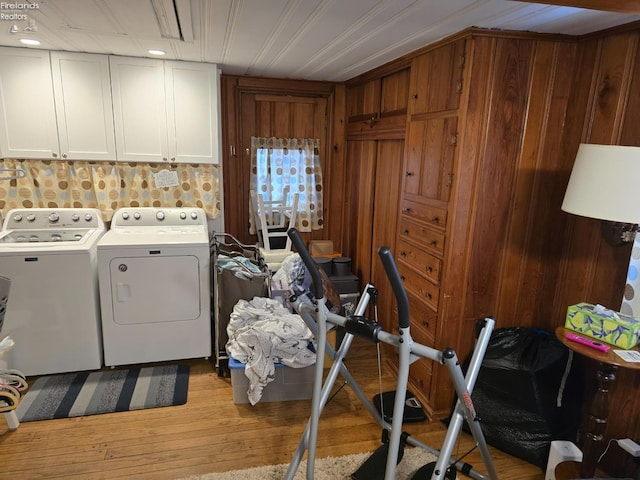 laundry room featuring light wood-style floors, cabinet space, wooden walls, and washing machine and clothes dryer