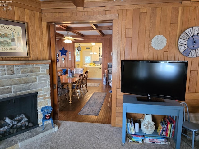 living area featuring beam ceiling, wood walls, a stone fireplace, wood finished floors, and coffered ceiling