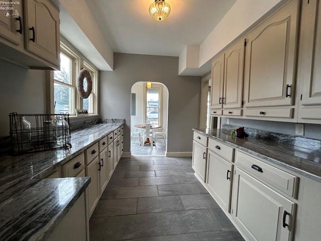 kitchen with arched walkways, baseboards, and dark stone countertops