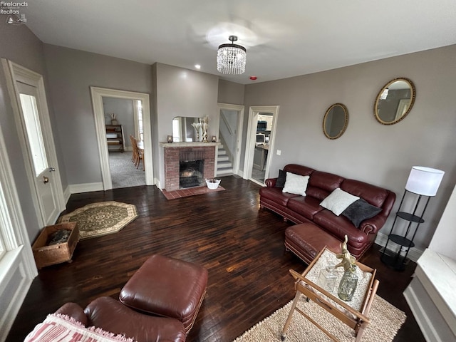 living room with a brick fireplace, baseboards, hardwood / wood-style floors, and an inviting chandelier