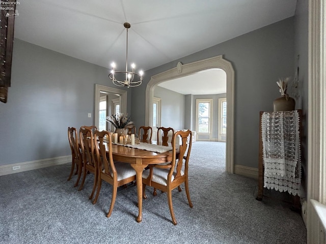 carpeted dining room with arched walkways, a notable chandelier, and baseboards