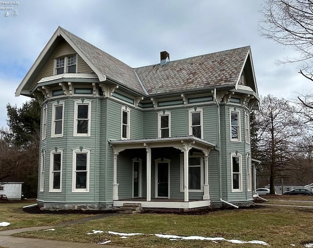 view of front of property featuring covered porch, a chimney, and a front yard