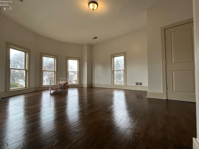 empty room featuring dark wood-type flooring, visible vents, and baseboards