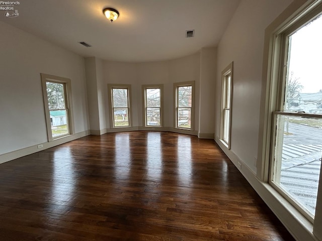 empty room with dark wood-style floors, baseboards, and visible vents