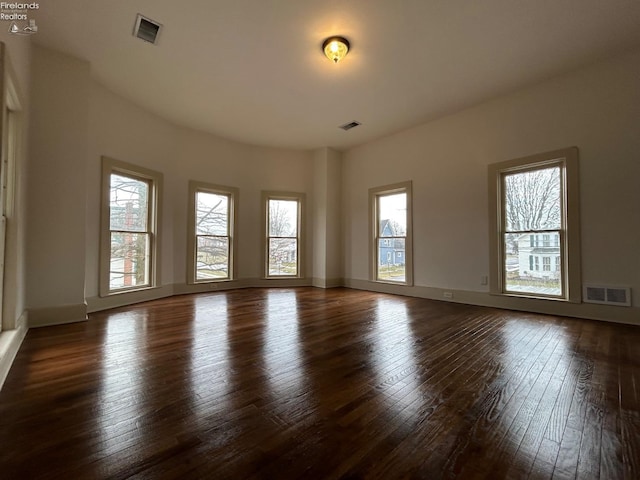 empty room featuring dark wood-type flooring, visible vents, and baseboards