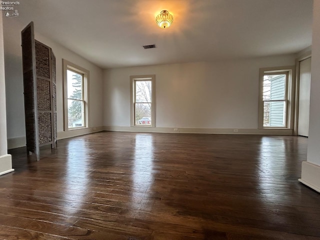 spare room featuring baseboards, visible vents, and dark wood-type flooring