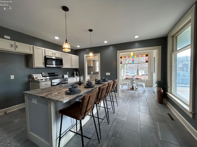 kitchen featuring an island with sink, baseboards, white cabinetry, and stainless steel appliances