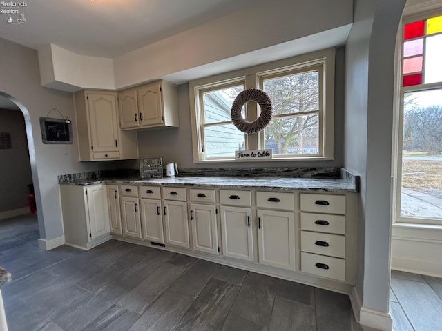 kitchen with arched walkways, stone counters, dark wood-style floors, and a healthy amount of sunlight