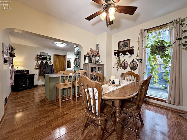 dining room with arched walkways, dark wood-style floors, a ceiling fan, and baseboards