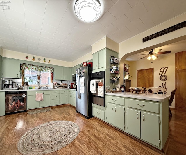 kitchen featuring dishwashing machine, light wood-style flooring, a peninsula, stainless steel refrigerator with ice dispenser, and green cabinetry