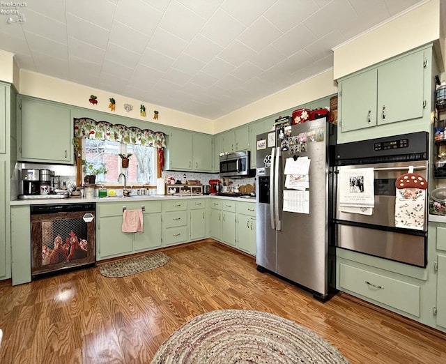 kitchen featuring a sink, appliances with stainless steel finishes, green cabinetry, and wood finished floors