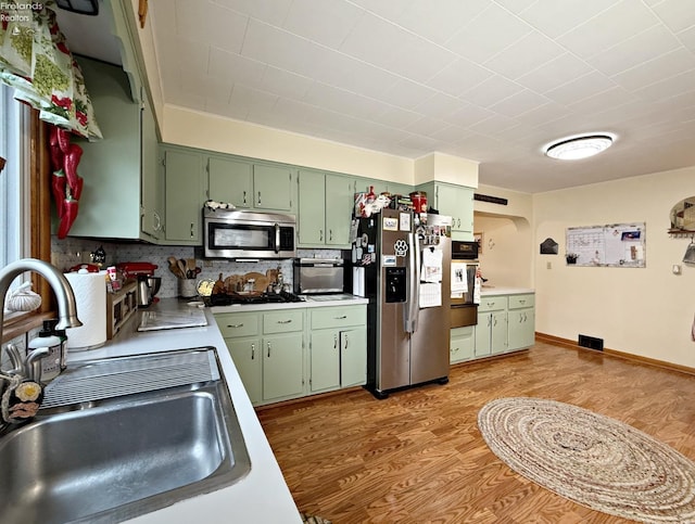 kitchen featuring appliances with stainless steel finishes, a sink, light wood finished floors, and green cabinets