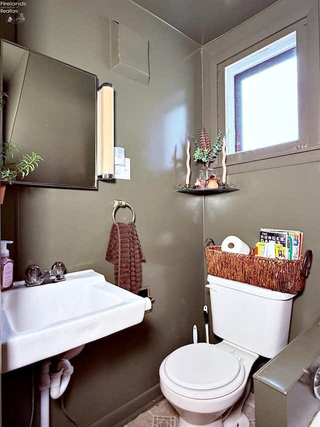 half bath with toilet, baseboards, and a sink