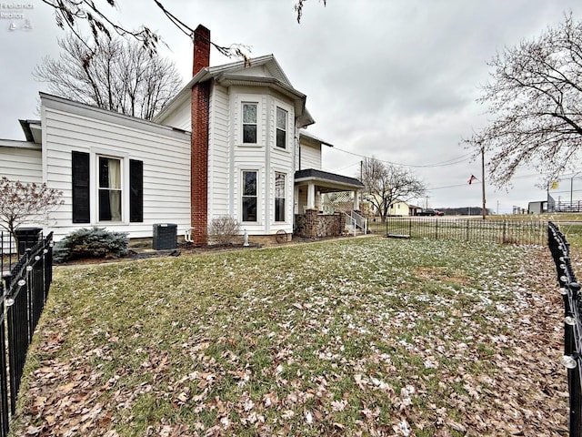 back of property with a fenced backyard, a chimney, central AC, and a yard