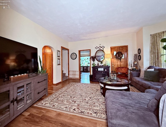 living area featuring arched walkways, stairway, and wood finished floors