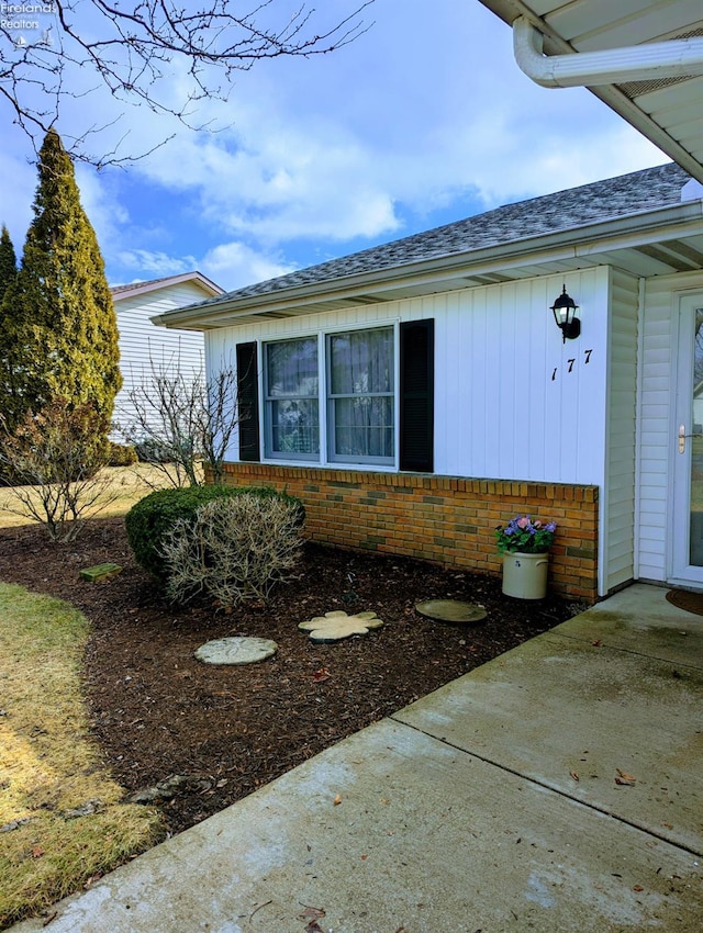 view of side of home featuring a shingled roof and brick siding