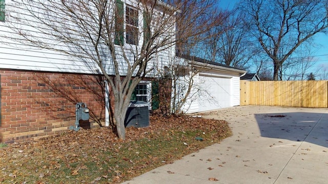 view of side of property featuring a garage, concrete driveway, brick siding, and fence