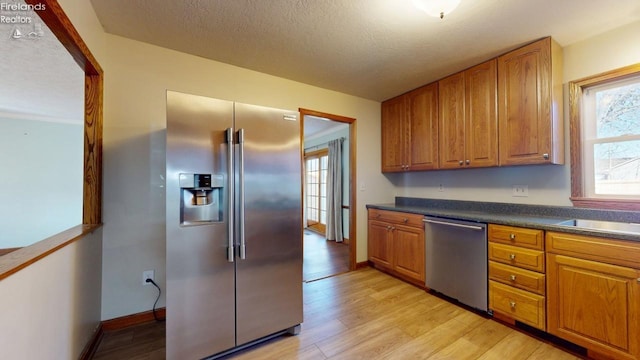 kitchen with dark countertops, light wood-style floors, appliances with stainless steel finishes, and brown cabinets