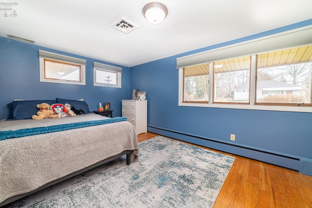 bedroom with a baseboard heating unit, visible vents, and wood finished floors