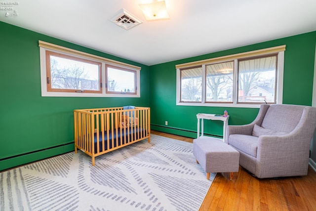 bedroom featuring a baseboard radiator, a baseboard heating unit, visible vents, baseboards, and wood-type flooring