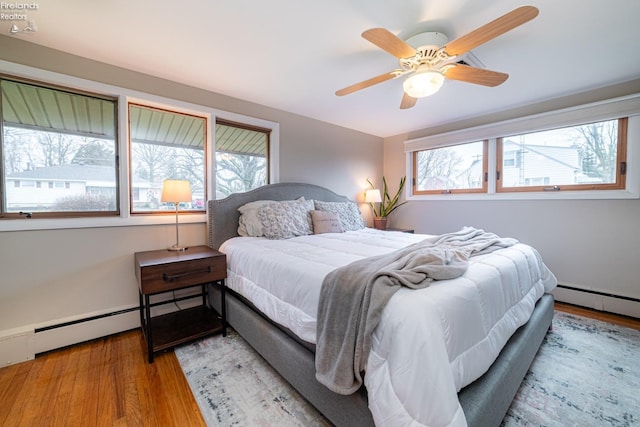 bedroom with multiple windows, ceiling fan, baseboard heating, and wood finished floors