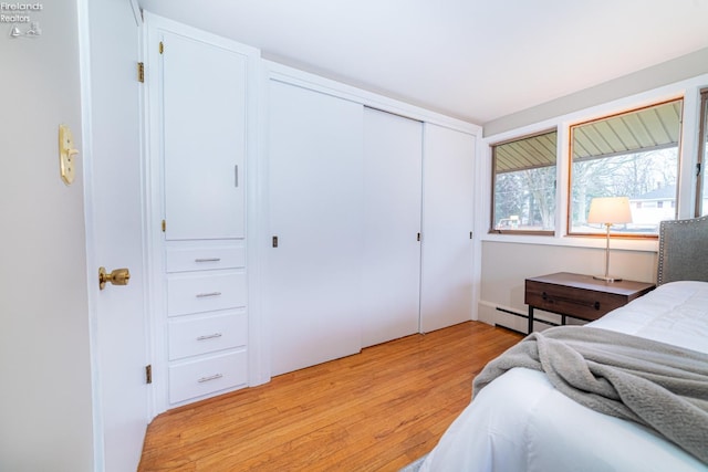 bedroom featuring light wood finished floors, baseboard heating, and a closet