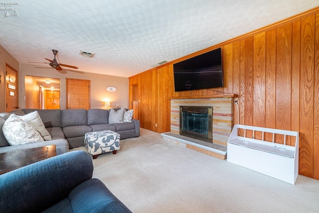 living room featuring visible vents, a glass covered fireplace, carpet flooring, wooden walls, and a textured ceiling