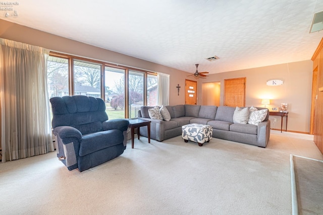 living area with a textured ceiling, baseboards, visible vents, and light colored carpet