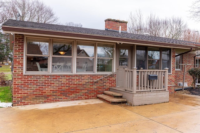 view of front of property with a shingled roof, a chimney, and brick siding