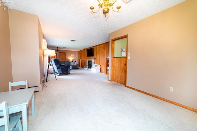 living area featuring light colored carpet, a fireplace with raised hearth, wooden walls, a textured ceiling, and a chandelier