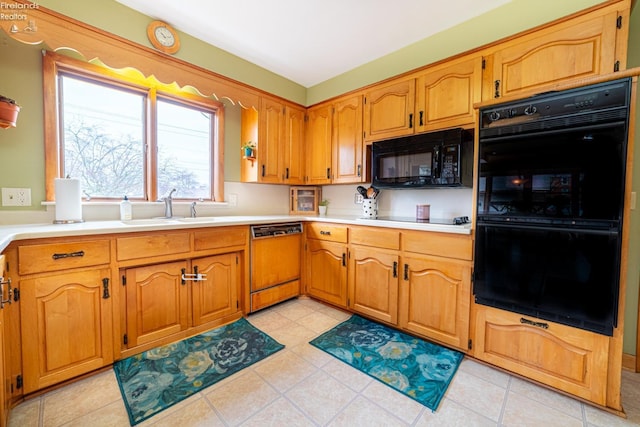 kitchen with brown cabinets, light countertops, black appliances, a sink, and light tile patterned flooring