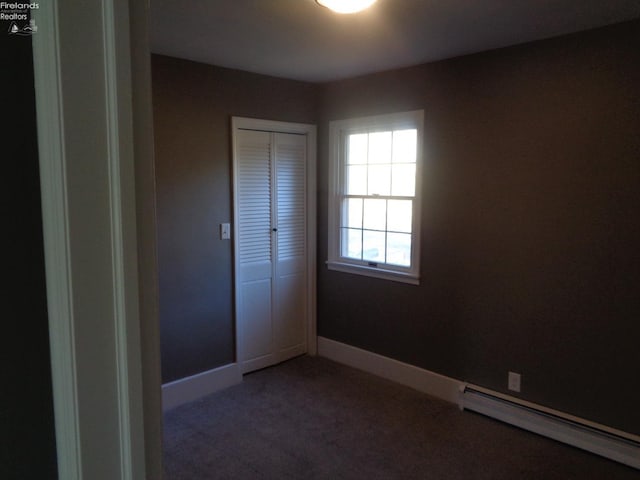 unfurnished bedroom with carpet floors, a closet, a baseboard radiator, and baseboards