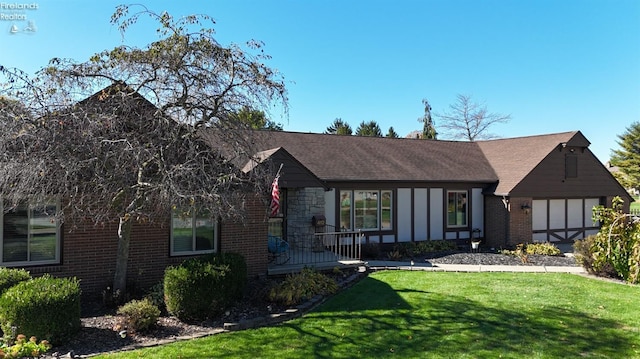 tudor home with a shingled roof, a front yard, and brick siding