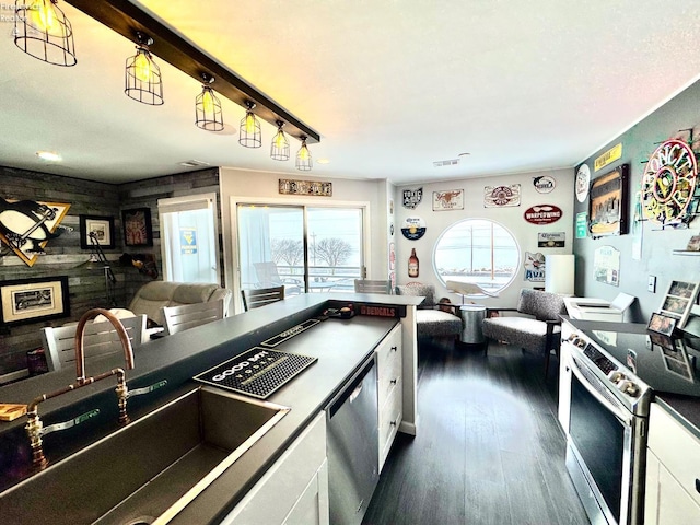 kitchen featuring dark wood finished floors, stainless steel appliances, open floor plan, white cabinets, and a sink