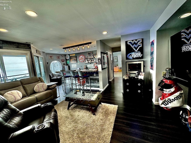 living room featuring rail lighting, visible vents, a bar, wood finished floors, and baseboards