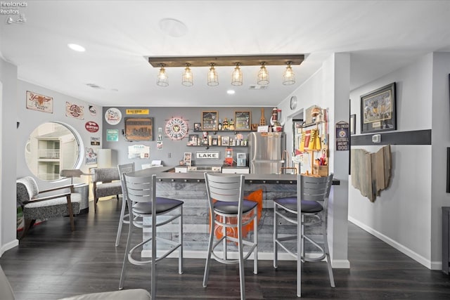 kitchen with a breakfast bar, dark wood finished floors, freestanding refrigerator, and baseboards