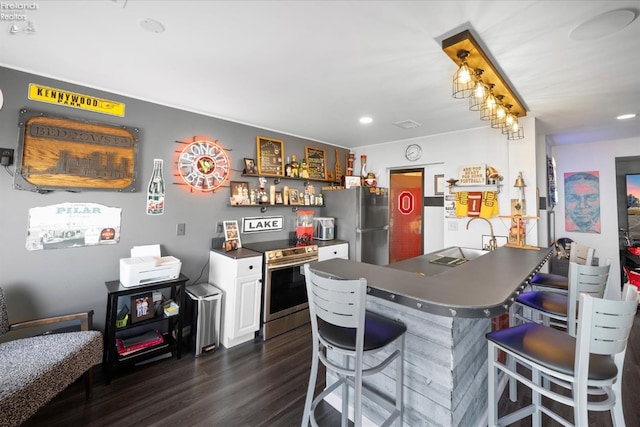 kitchen with a breakfast bar area, dark countertops, appliances with stainless steel finishes, dark wood-type flooring, and a peninsula