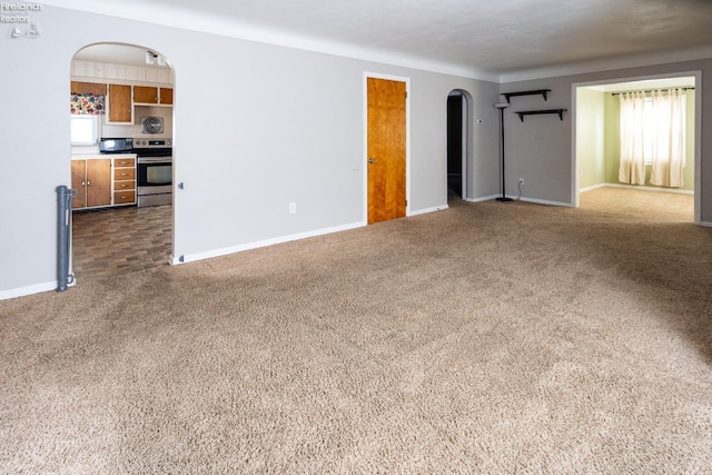 unfurnished living room with arched walkways, carpet, and baseboards