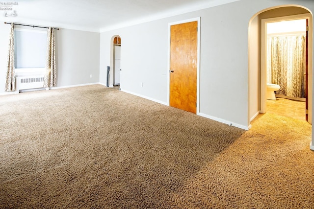 carpeted empty room featuring arched walkways, radiator, and baseboards