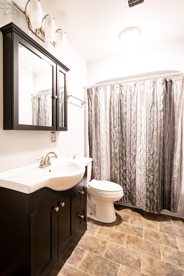 full bath with toilet, stone finish floor, and vanity