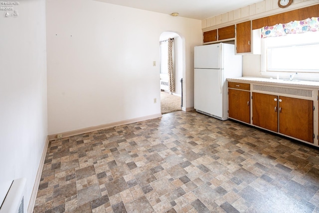 kitchen with arched walkways, baseboards, freestanding refrigerator, and brown cabinets