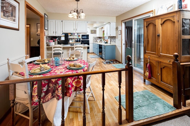 dining room with light wood-style flooring, a textured ceiling, and a notable chandelier