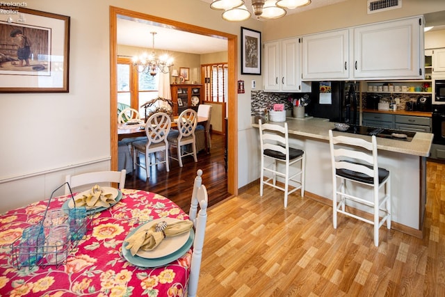 kitchen with visible vents, light wood-style flooring, white cabinetry, a chandelier, and black appliances